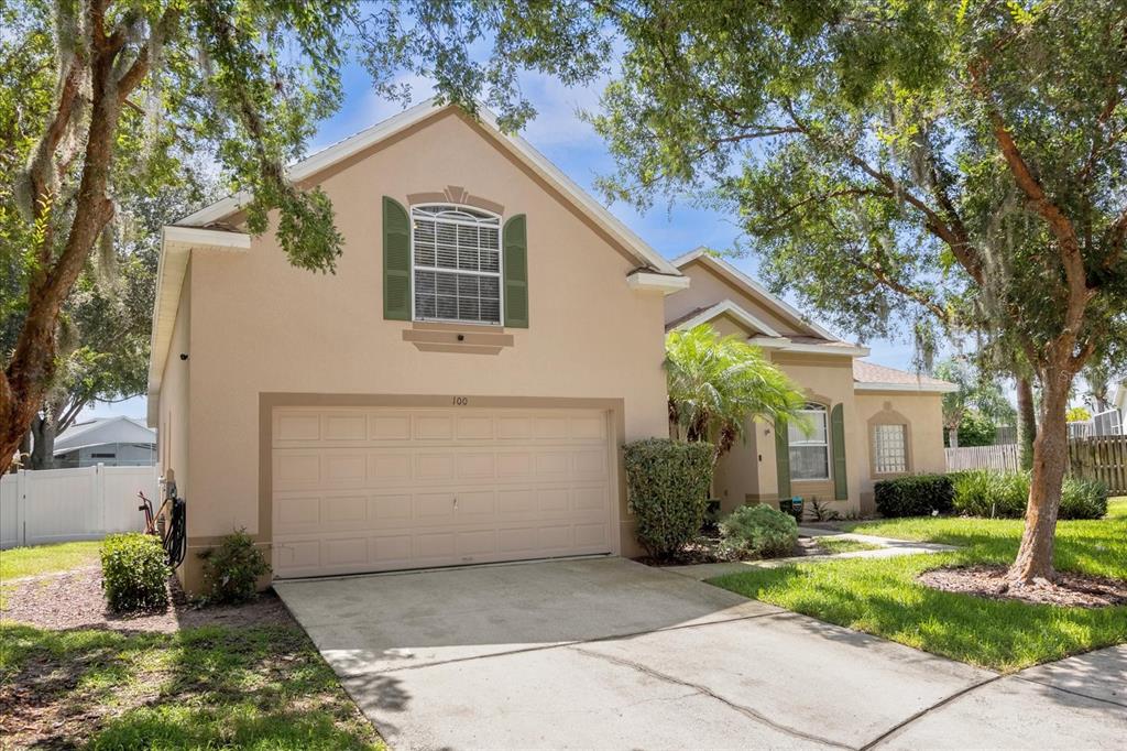 A tan two-story house with a two-car garage, green shutters, and a concrete driveway — 100 HOLLYBROOK COURT, DAVENPORT, FL
