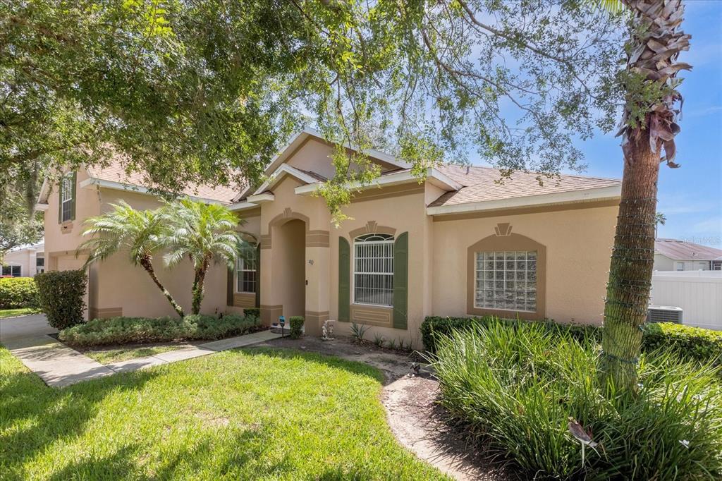 A single-story tan house with a glass block window, green shutters, and a palm tree — 100 HOLLYBROOK COURT, DAVENPORT, FL