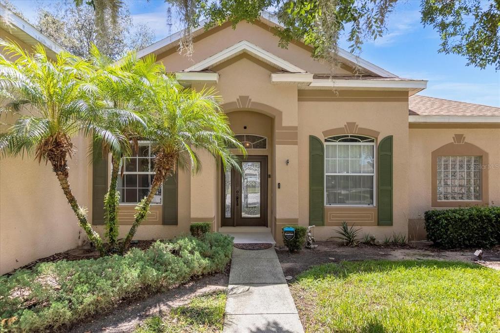 A tan single-story house features a front walkway, palm trees, and green shutters — 100 HOLLYBROOK COURT, DAVENPORT, FL