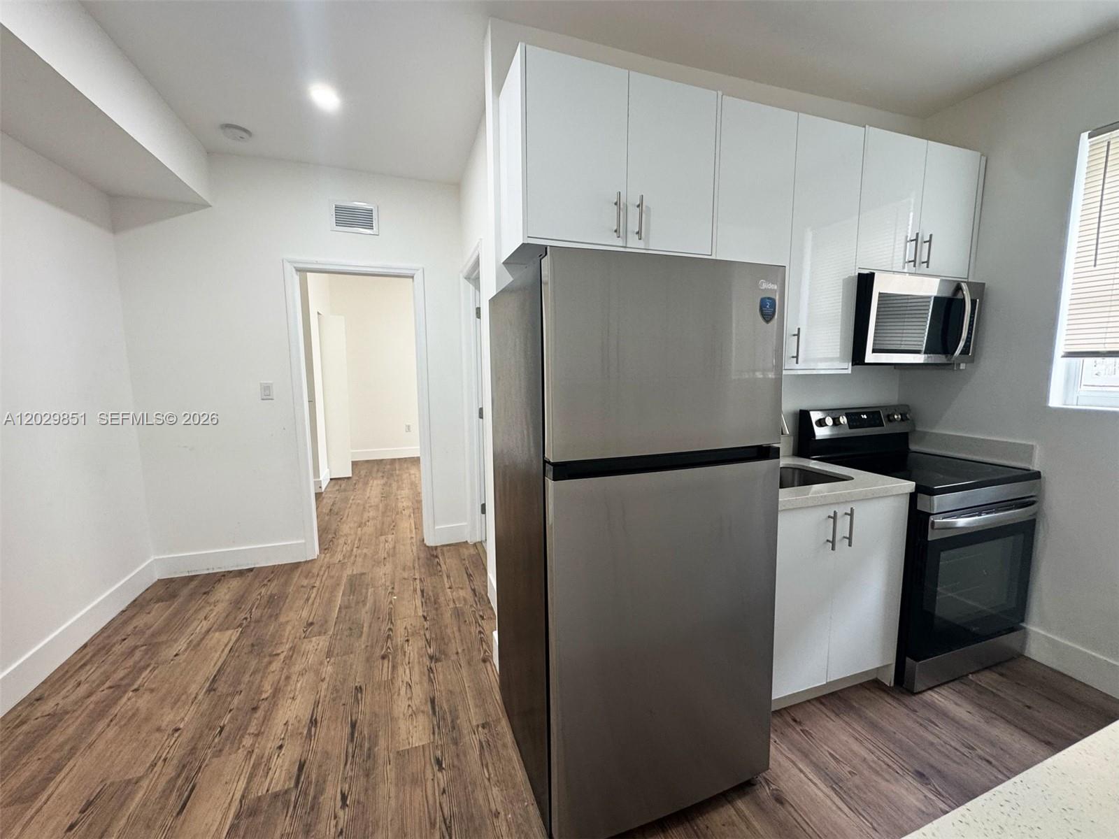 A kitchen features white cabinets, stainless steel appliances, and wood-look flooring — 321 SW 9th Ave # 4, Miami FL 33130, MIAMI, FL
