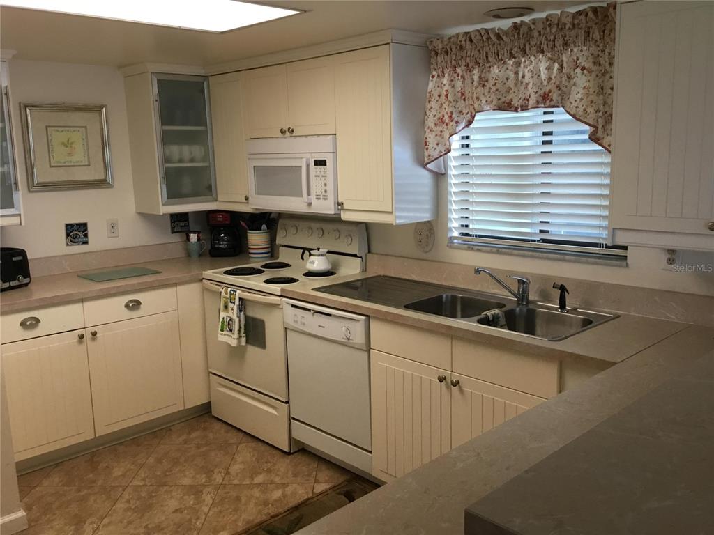 A kitchen features white cabinets, a white stove, a double sink, and beige countertops — 1571 S ATLANTIC AVENUE UNIT 308, NEW SMYRNA BEACH, FL