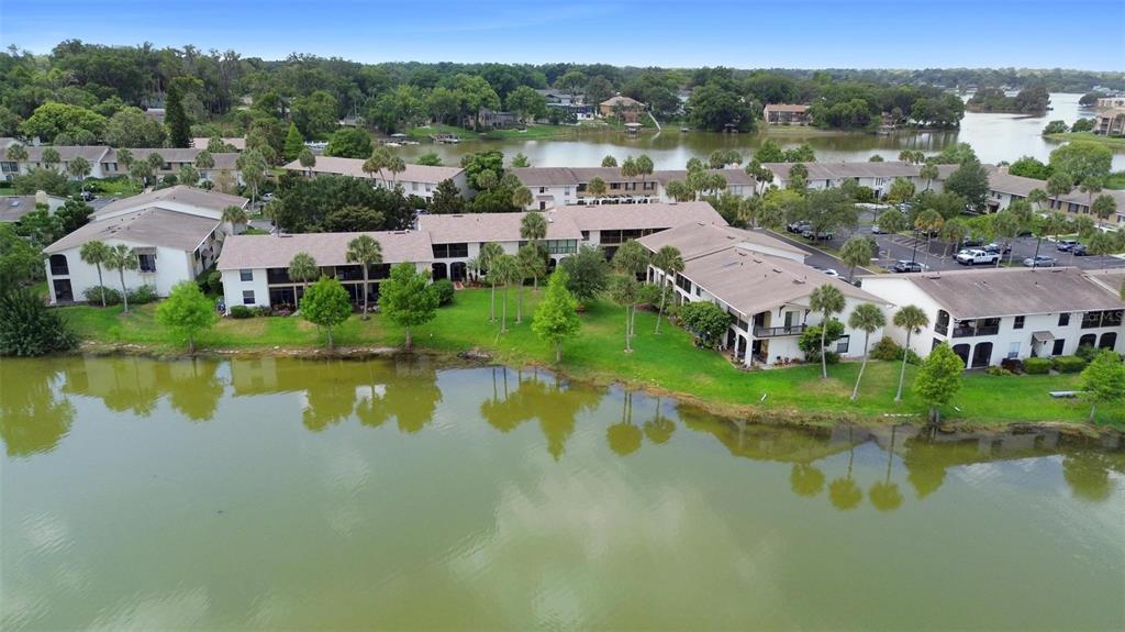 An aerial view shows multi-story apartment buildings situated along the edge of a lake — 200 MAITLAND AVENUE UNIT 174, ALTAMONTE SPRINGS, FL