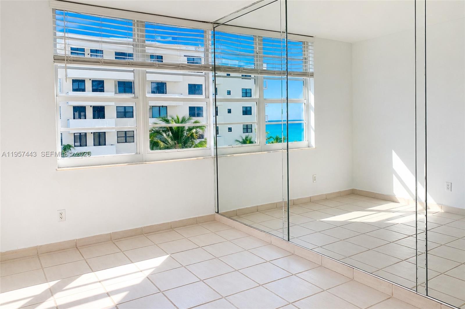 An empty room with tiled floors, mirrored walls, and windows overlooking a building and ocean — 100 Lincoln Rd # 732, Miami Beach FL 33139, MIAMI BEACH, FL