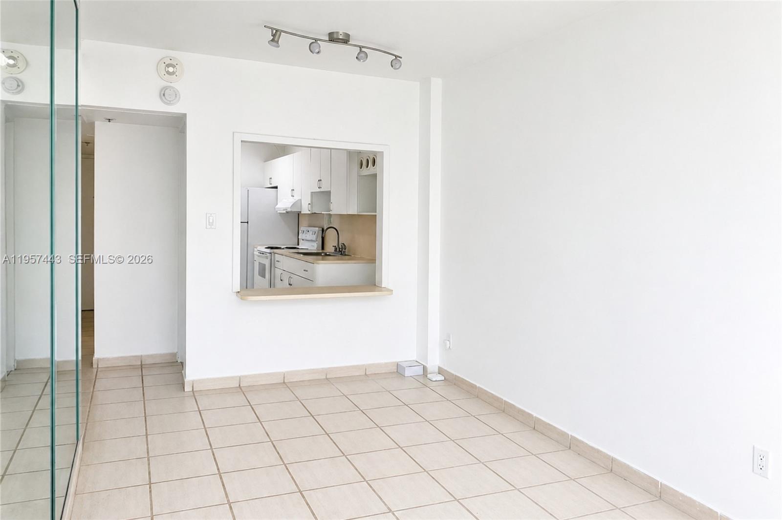An empty room with tiled floors features a kitchen pass-through window and track lighting — 100 Lincoln Rd # 732, Miami Beach FL 33139, MIAMI BEACH, FL