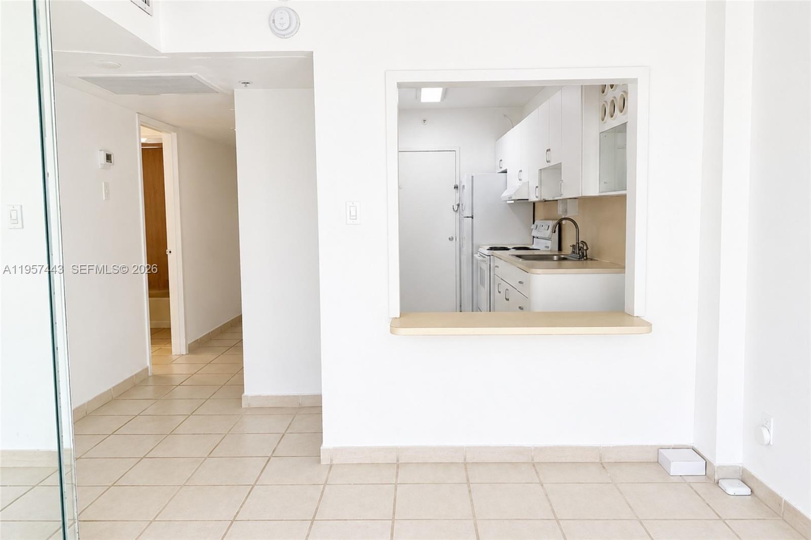 A white kitchen with a pass-through window overlooks a tiled living area — 100 Lincoln Rd # 732, Miami Beach FL 33139, MIAMI BEACH, FL