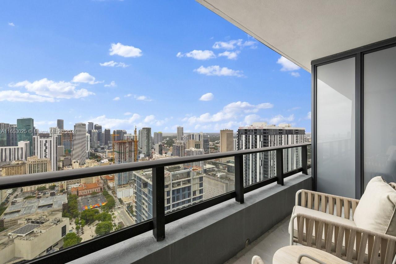 A high-rise balcony features outdoor seating overlooking a dense urban skyline under a blue sky — 601 NE 1 # 4410, Miami FL 33132, MIAMI, FL