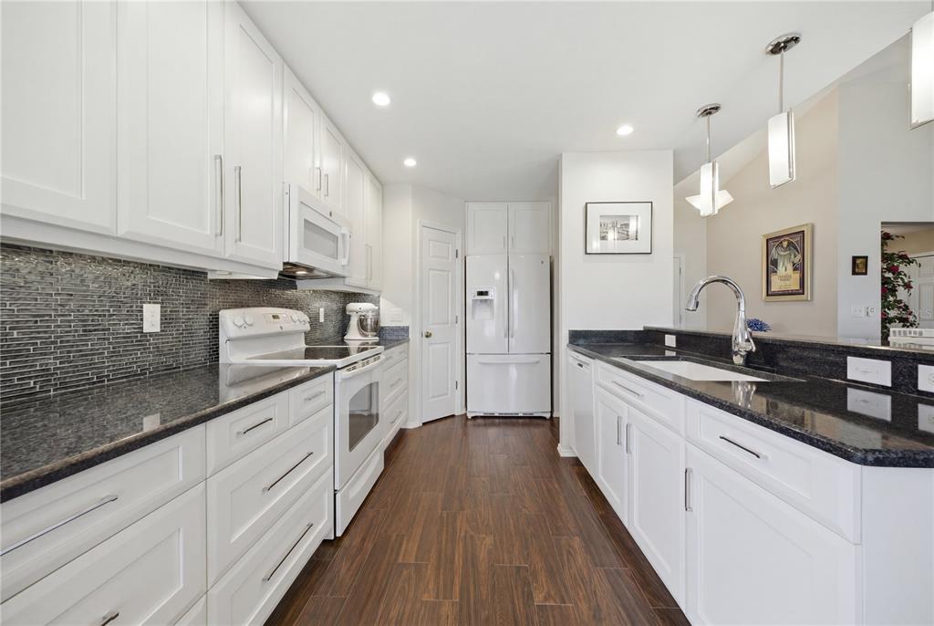 A kitchen features white cabinetry, dark granite countertops, a tiled backsplash, and wood-look flooring — 4226 KINGSFIELD DRIVE, PARRISH, FL