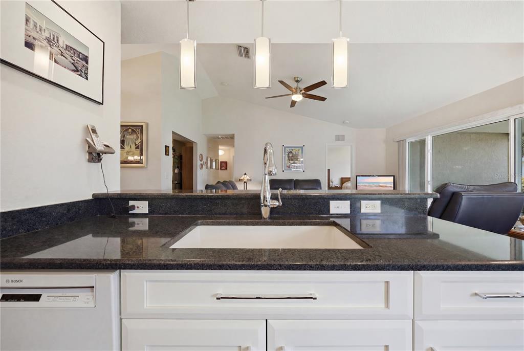 A kitchen sink and countertop overlook a living area with white cabinets and pendant lighting — 4226 KINGSFIELD DRIVE, PARRISH, FL