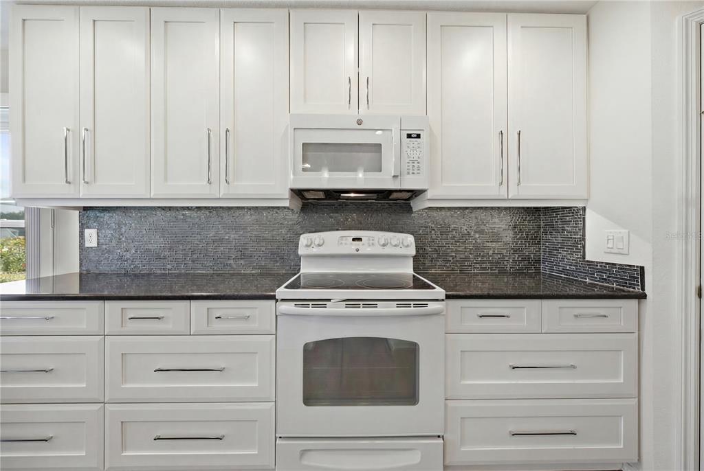 A kitchen features white cabinets, a dark countertop, a tiled backsplash, and white appliances — 4226 KINGSFIELD DRIVE, PARRISH, FL
