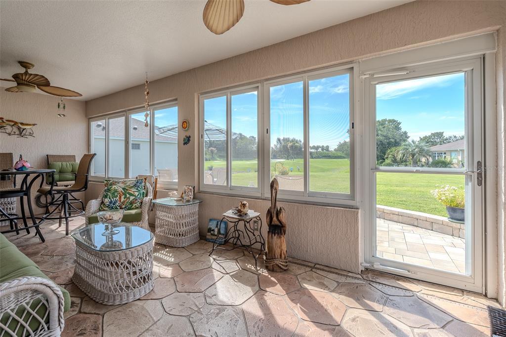 A sunroom with stone flooring, wicker furniture, and large windows overlooking a grassy golf course — 15541 SW 11TH TERRACE ROAD, OCALA, FL