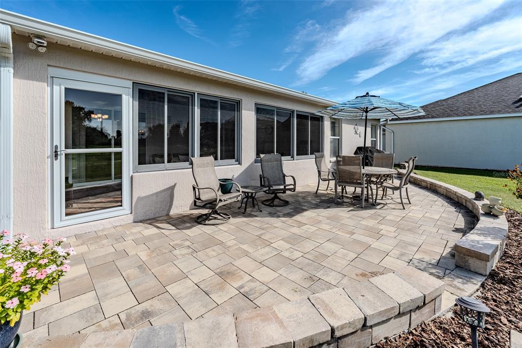 A paved patio with outdoor furniture sits beside a house with a glass sliding door — 15541 SW 11TH TERRACE ROAD, OCALA, FL