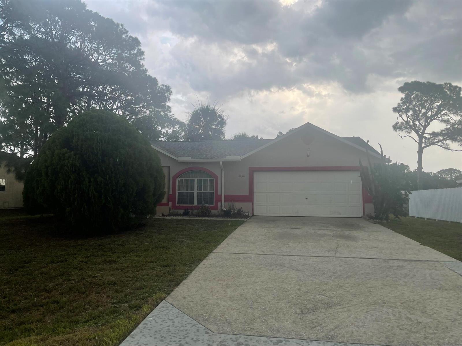 A single-story house with a white garage door, beige stucco walls, and red trim accents — 3968 Jupiter Boulevard SE, Palm Bay FL 32909, PALM BAY, FL