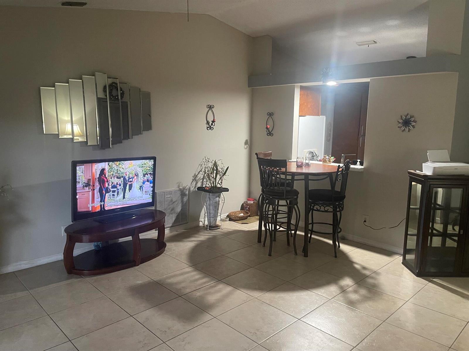 A living room with tile flooring, a television on a stand, and a dining area — 3968 Jupiter Boulevard SE, Palm Bay FL 32909, PALM BAY, FL