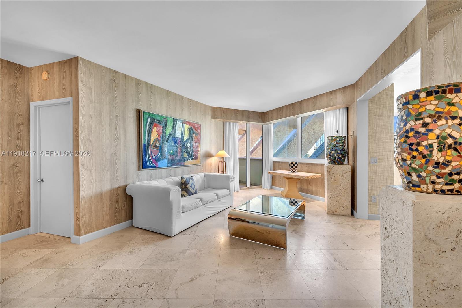 A living room features wood-paneled walls, a white sofa, a glass coffee table, and tile flooring — 300 S Pointe Dr # 906, Miami Beach FL 33139, MIAMI BEACH, FL