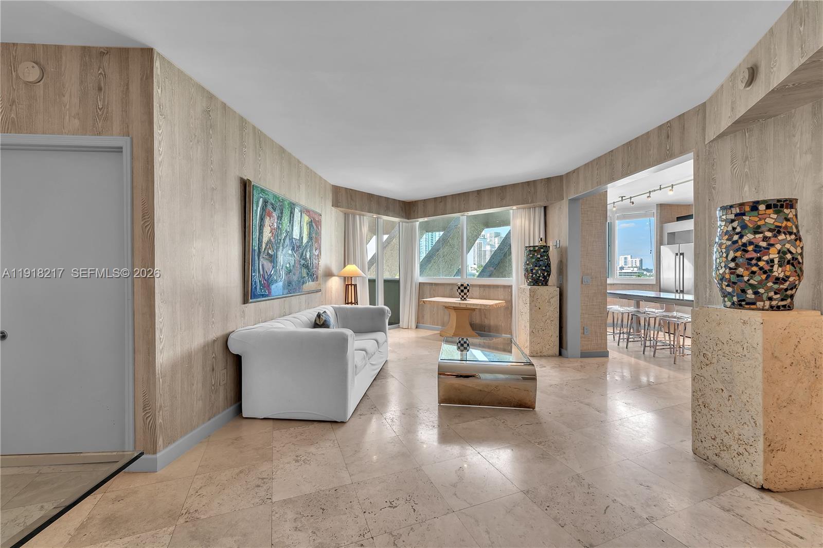 A living room features wood-paneled walls, tile flooring, a white sofa, and a glass coffee table — 300 S Pointe Dr # 906, Miami Beach FL 33139, MIAMI BEACH, FL