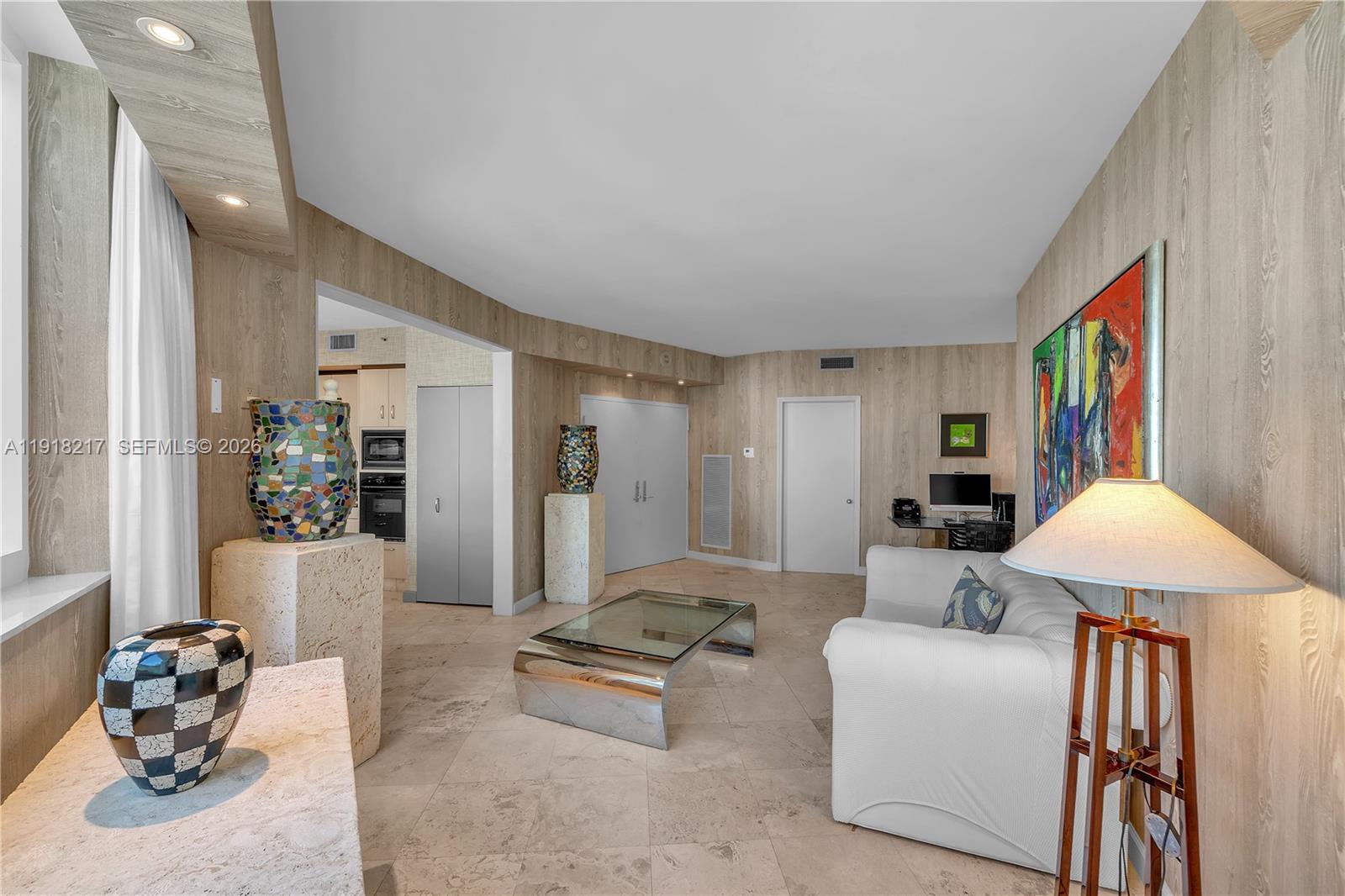 A living room features wood-paneled walls, tile flooring, a white sofa, and decorative vases — 300 S Pointe Dr # 906, Miami Beach FL 33139, MIAMI BEACH, FL