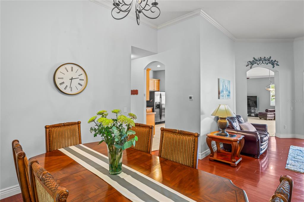 A dining room with a wooden table, striped runner, and wall clock leads to a kitchen — 12801 STANWYCK CIRCLE, TAMPA, FL