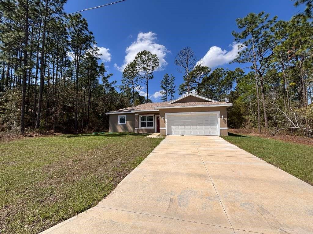 A single-story house with a beige exterior, white garage door, and a concrete driveway — 7908 N GALENA AVENUE, DUNNELLON, FL