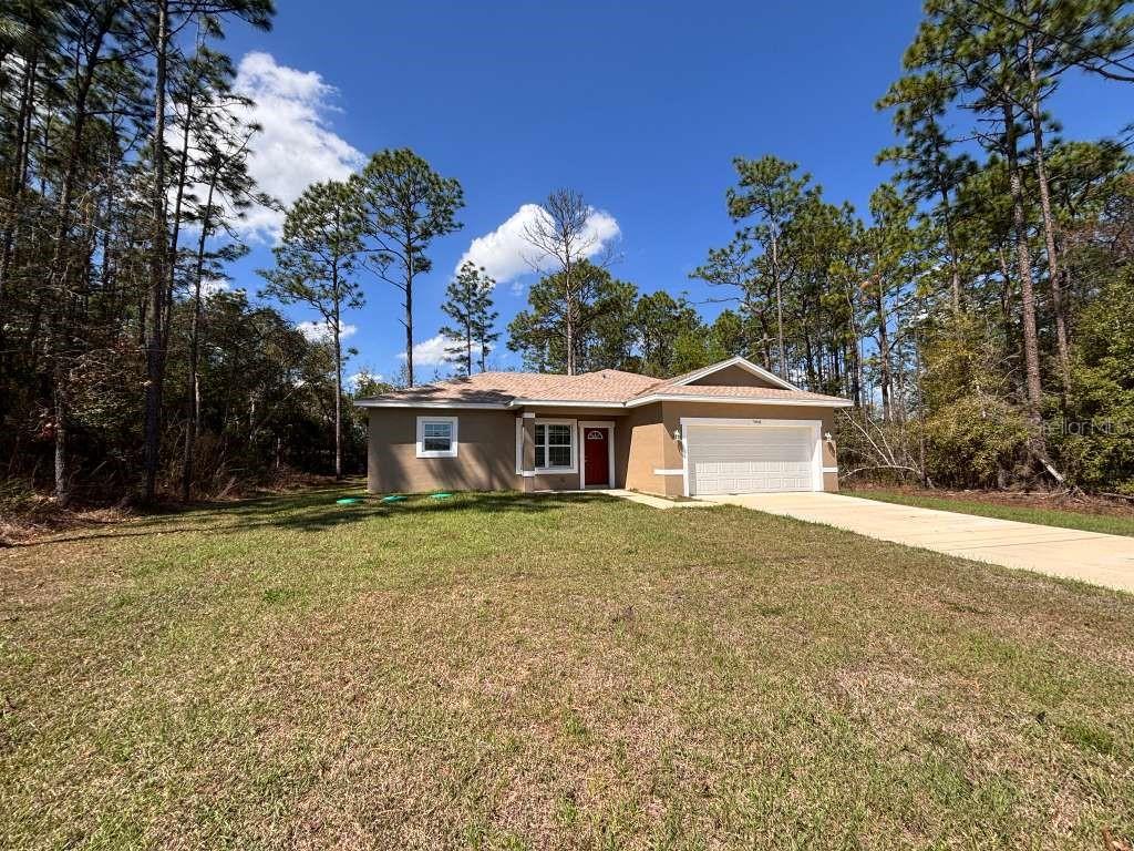 A single-story house with a tan exterior, red front door, and a two-car garage — 7908 N GALENA AVENUE, DUNNELLON, FL