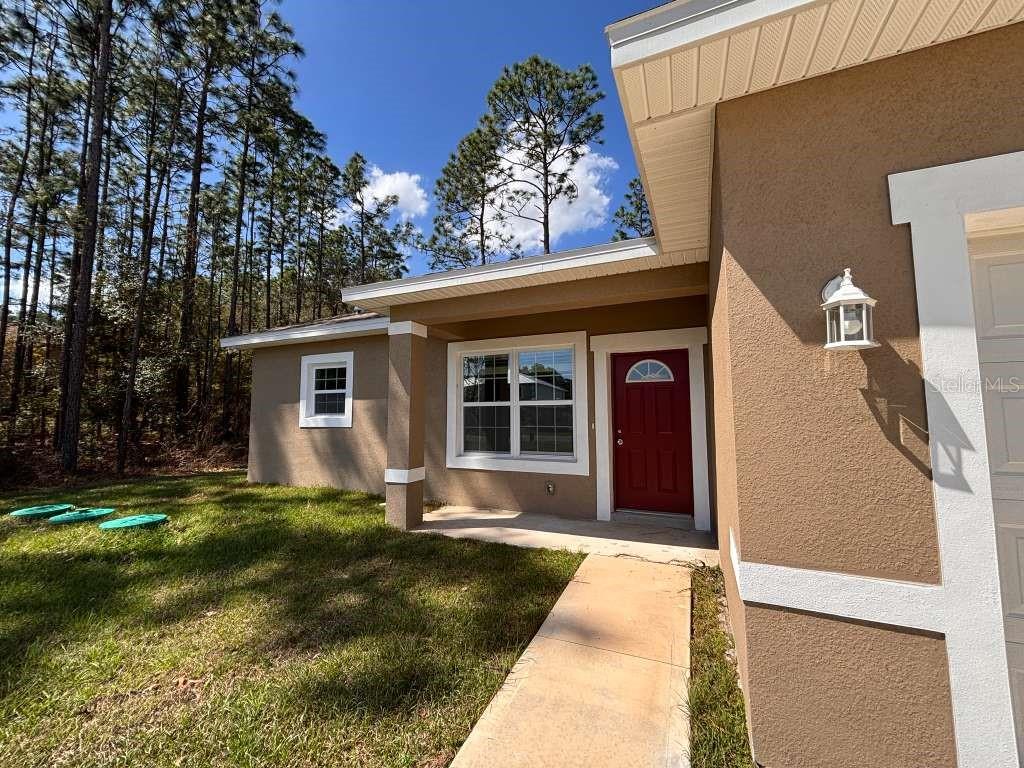 A tan stucco house exterior features a red front door and a concrete walkway — 7908 N GALENA AVENUE, DUNNELLON, FL