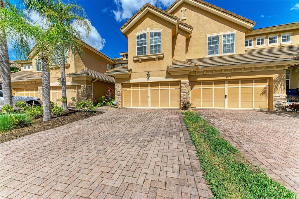 A two-story tan stucco townhouse with a paved driveway and two attached garage doors — 8160 VILLA GRANDE CT, SARASOTA, FL