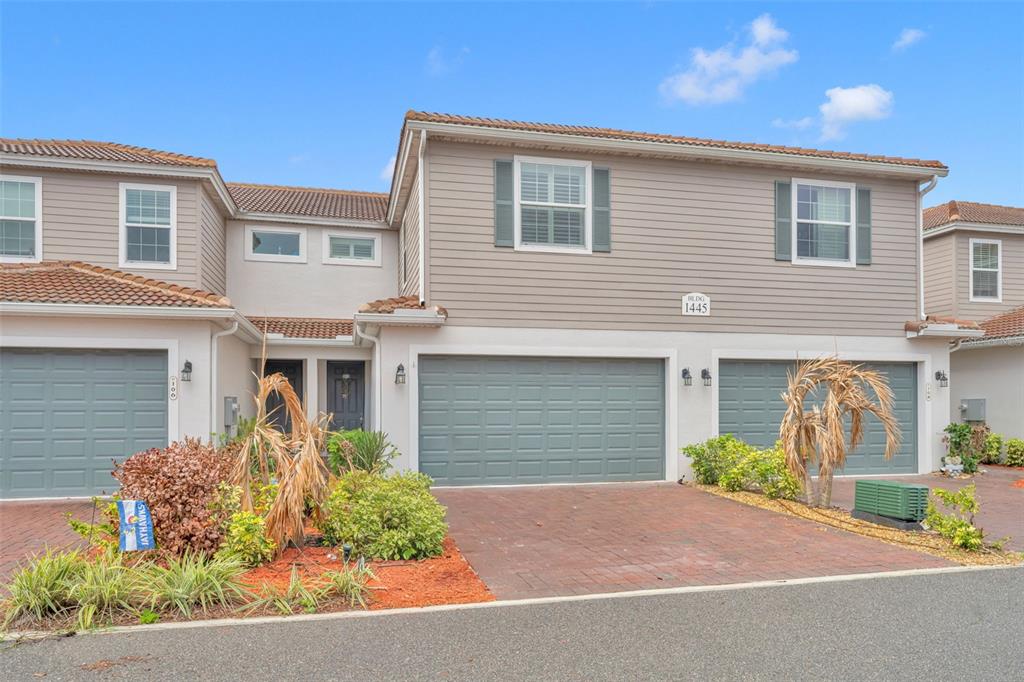 A multi-unit residential building with beige siding, gray garage doors, and a brick driveway — 1445 ISABELLA DRIVE UNIT 105, MELBOURNE, FL