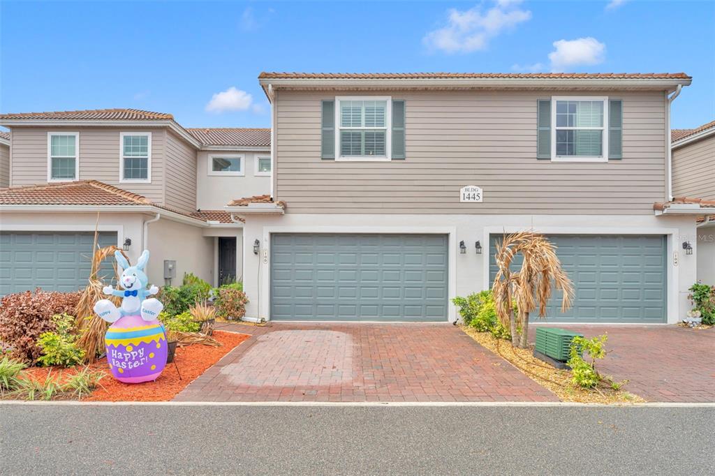 A two-story townhouse exterior features a brick driveway, two garage doors, and a lawn ornament — 1445 ISABELLA DRIVE UNIT 105, MELBOURNE, FL