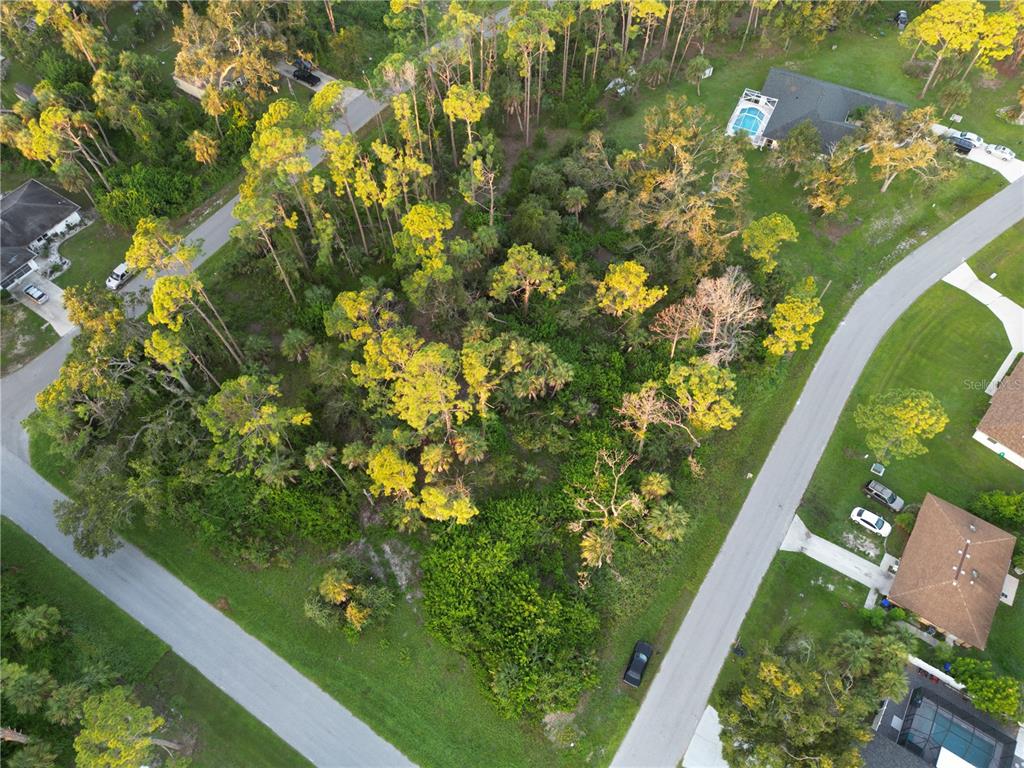 An aerial view shows a wooded, undeveloped residential lot situated between two paved streets — YUMA AVENUE, NORTH PORT, FL