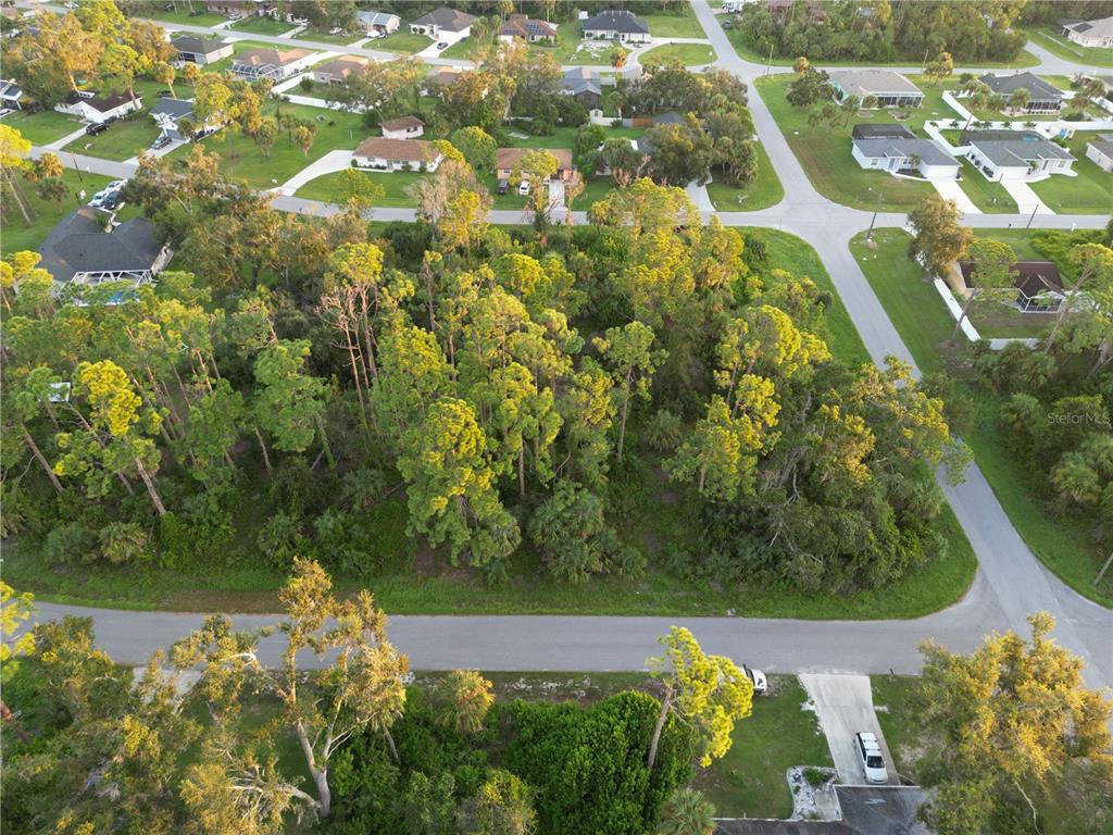 An aerial view shows a wooded, undeveloped residential lot surrounded by suburban houses and streets — YUMA AVENUE, NORTH PORT, FL
