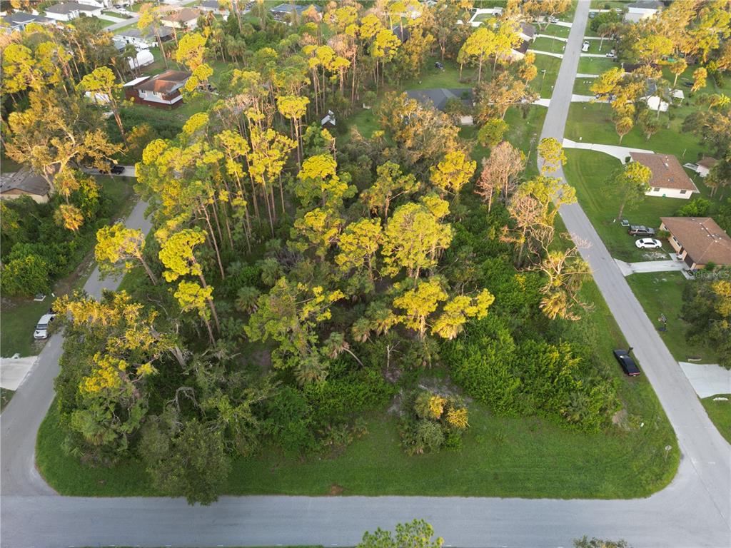 An aerial view shows a wooded, undeveloped residential lot surrounded by suburban houses and streets. on — YUMA AVENUE, NORTH PORT, FL
