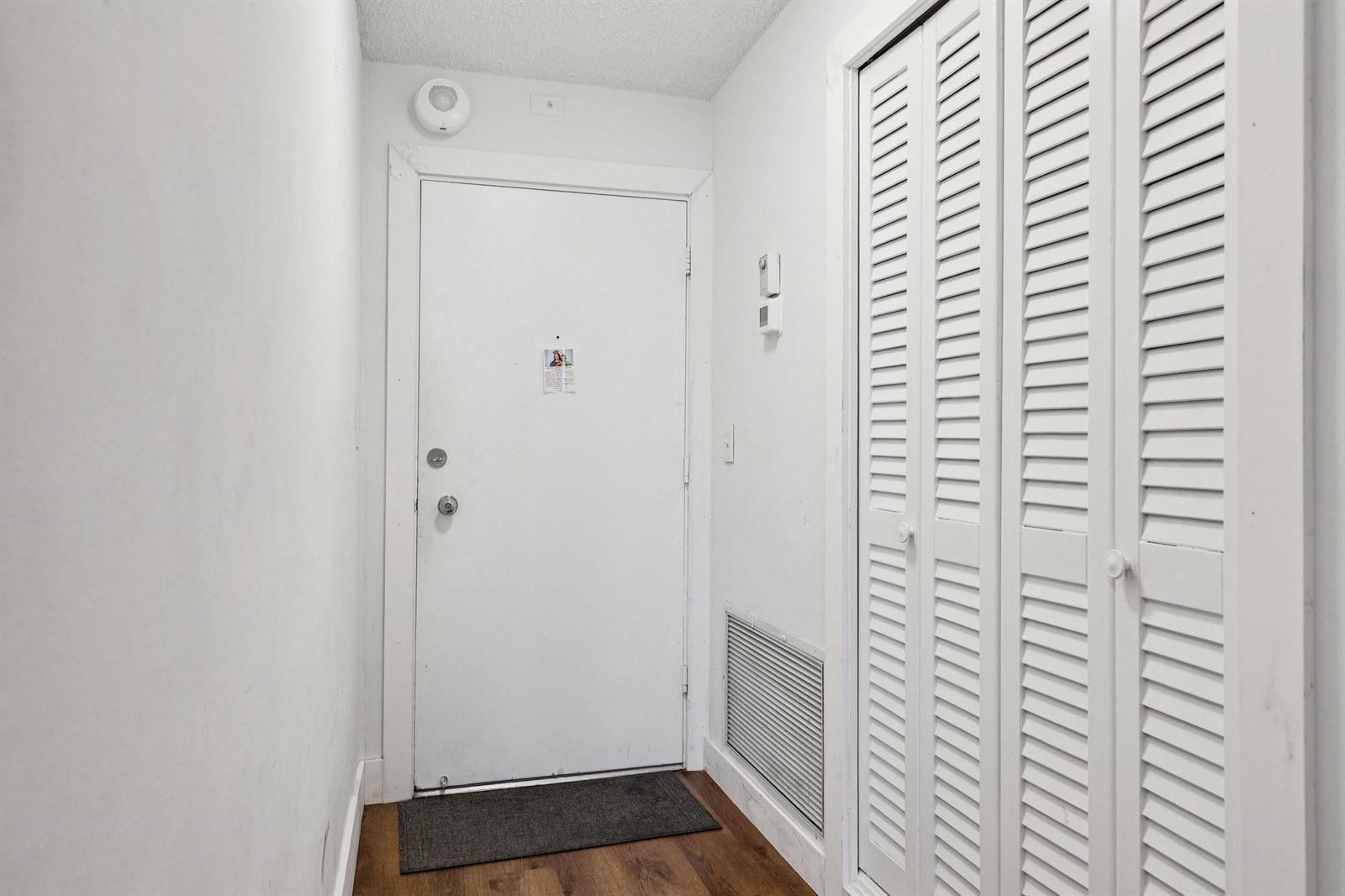 A white entry door with a closet featuring louvered doors and wood-look flooring — 133 N Pompano Beach Boulevard # 210, Pompano Beach FL 33062, POMPANO BEACH, FL