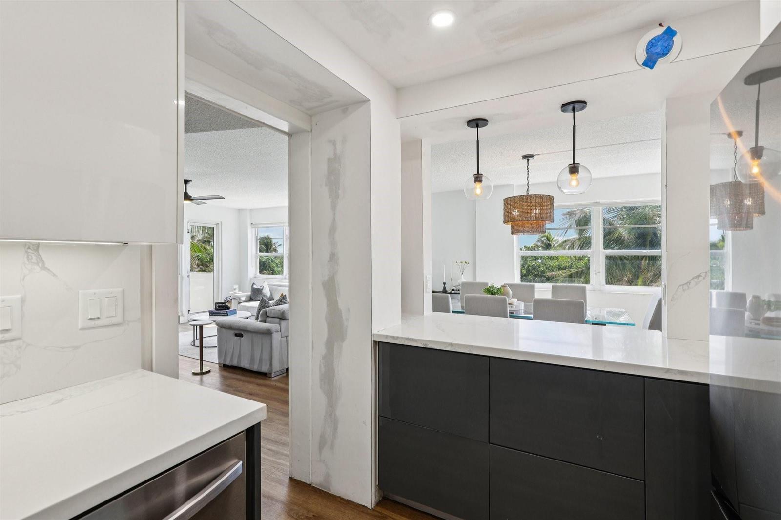 A kitchen with dark cabinets and white countertops looking into a dining area and living room — 133 N Pompano Beach Boulevard # 210, Pompano Beach FL 33062, POMPANO BEACH, FL