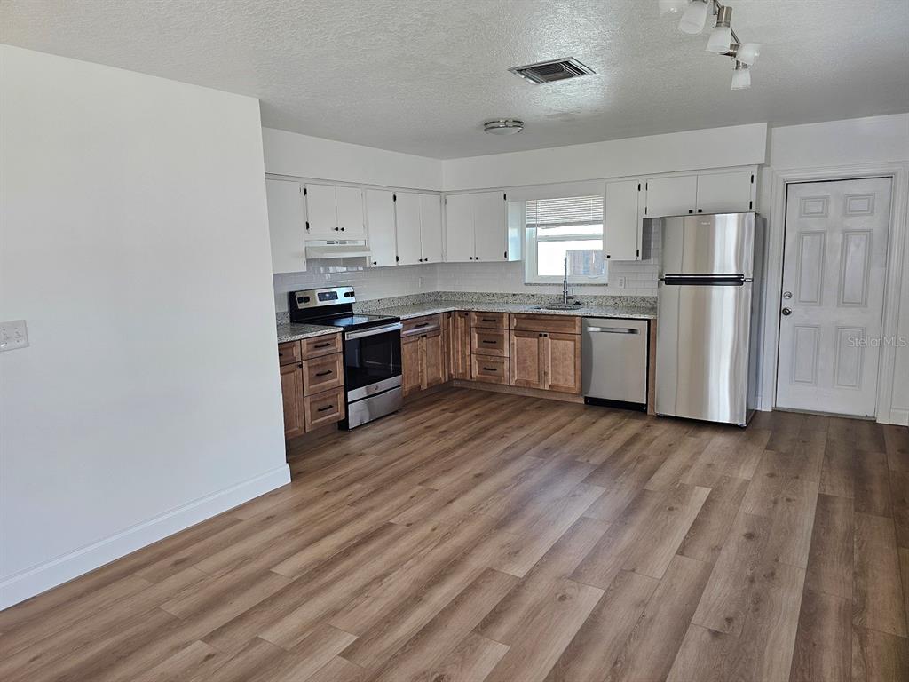 A kitchen features white upper cabinets, wood lower cabinets, stainless steel appliances, and wood-look flooring — 175 174TH TERRACE DRIVE E UNIT 2, REDINGTON SHORES, FL