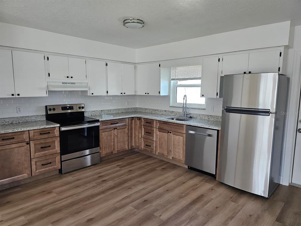 A kitchen features white upper cabinets, wood lower cabinets, granite countertops, and stainless steel appliances — 175 174TH TERRACE DRIVE E UNIT 2, REDINGTON SHORES, FL