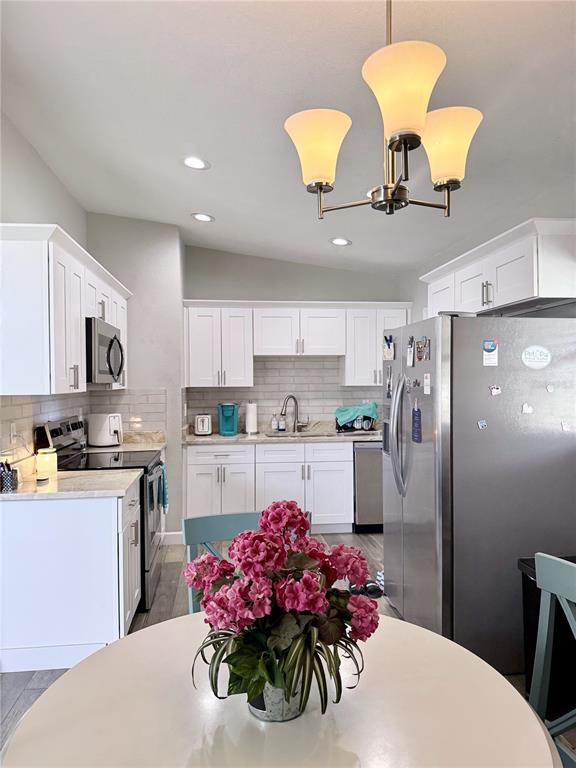 A kitchen features white cabinetry, stainless steel appliances, and a round dining table with flowers — 4497 MENHADEN DRIVE SE, ST PETERSBURG, FL