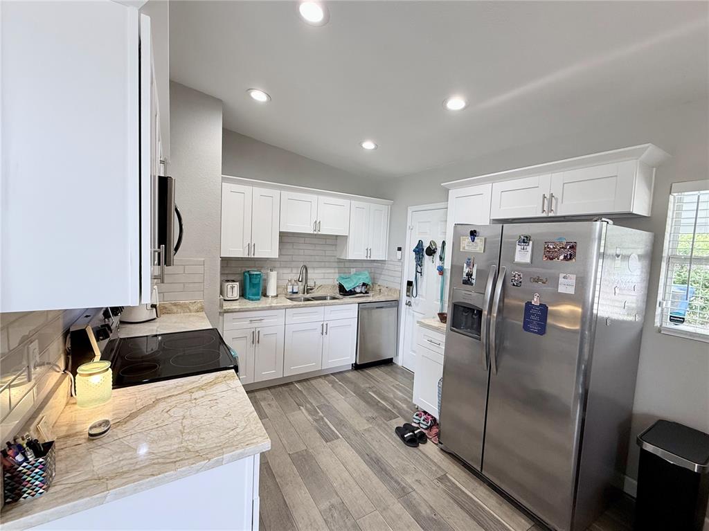 A kitchen features white cabinets, stainless steel appliances, granite countertops, and wood-look flooring — 4497 MENHADEN DRIVE SE, ST PETERSBURG, FL