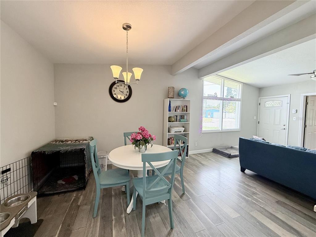 A dining area features a round white table, blue chairs, a dog crate, and wood-look flooring — 4497 MENHADEN DRIVE SE, ST PETERSBURG, FL