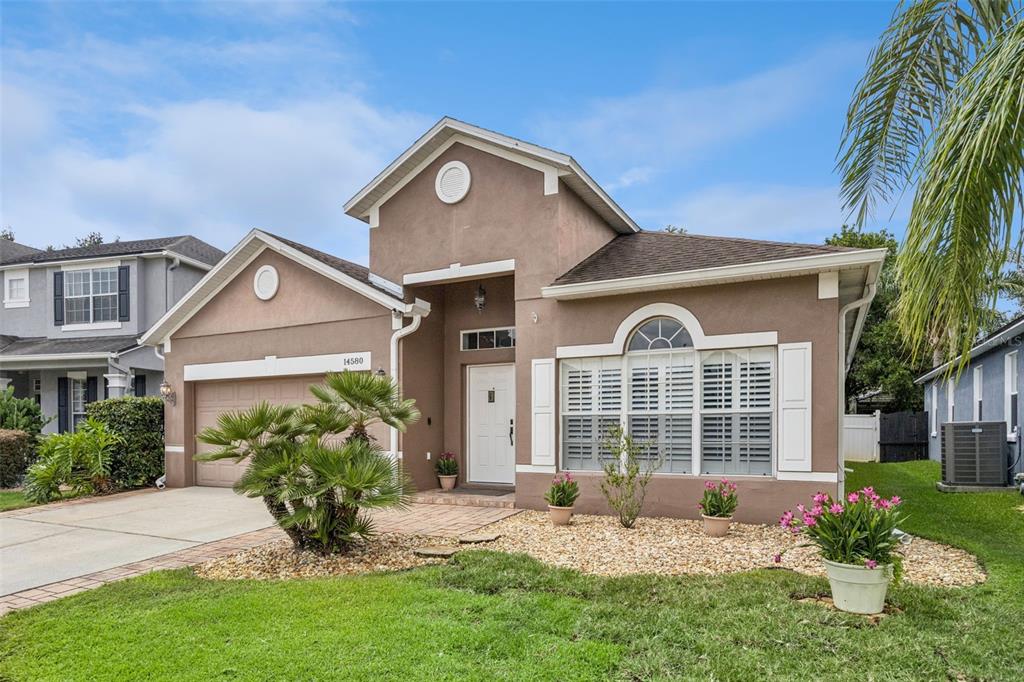 A tan single-story house with a two-car garage, a front porch, and landscaped garden beds — 14580 SAINT GEORGES HILL DRIVE, ORLANDO, FL