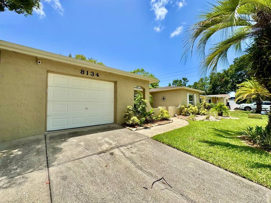 A single-story house with a white garage door, a concrete driveway, and a landscaped yard — 8134 WINTHROP DRIVE, PORT RICHEY, FL