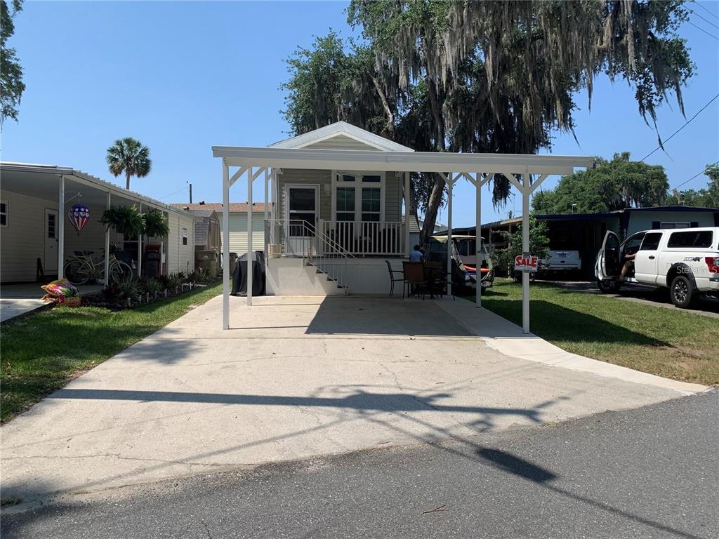 A small manufactured home features a large attached carport and a front porch with stairs — 699 CINDI AVENUE, LEESBURG, FL