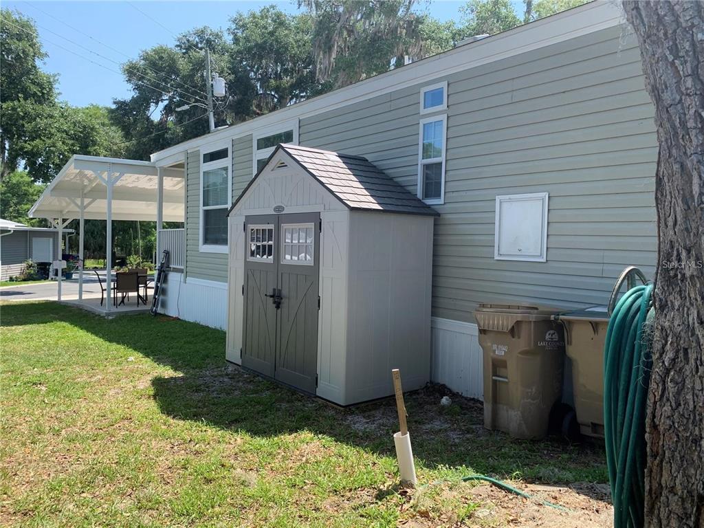 A light green mobile home exterior features a plastic storage shed and a covered patio — 699 CINDI AVENUE, LEESBURG, FL