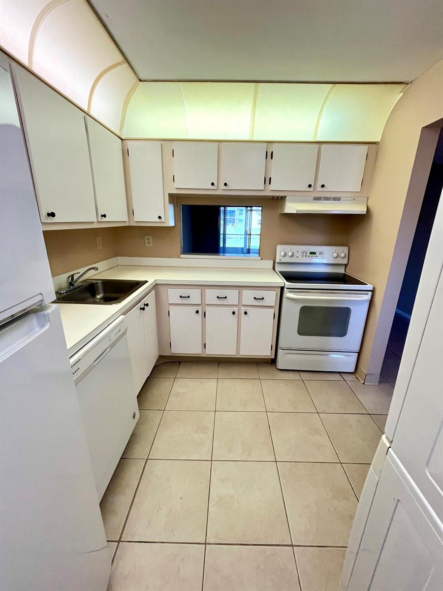 A kitchen features white cabinets, white appliances, beige tile flooring, and a pass-through window — 2500 Fiore Way # 1110, Delray Beach FL 33445, DELRAY BEACH, FL