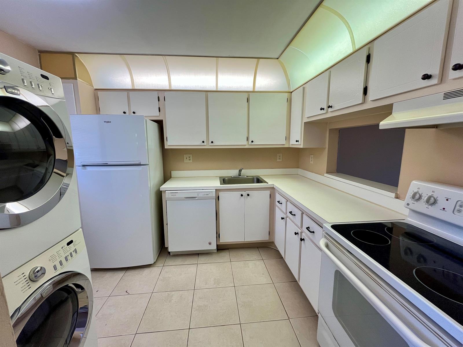 A kitchen features white appliances, white cabinetry, a stacked washer and dryer, and tile flooring — 2500 Fiore Way # 1110, Delray Beach FL 33445, DELRAY BEACH, FL