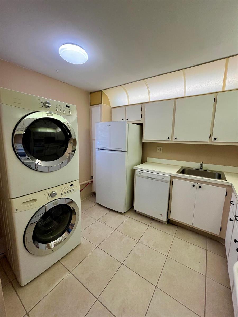 A kitchen features a stacked washer and dryer, white appliances, beige cabinets, and tiled flooring — 2500 Fiore Way # 1110, Delray Beach FL 33445, DELRAY BEACH, FL