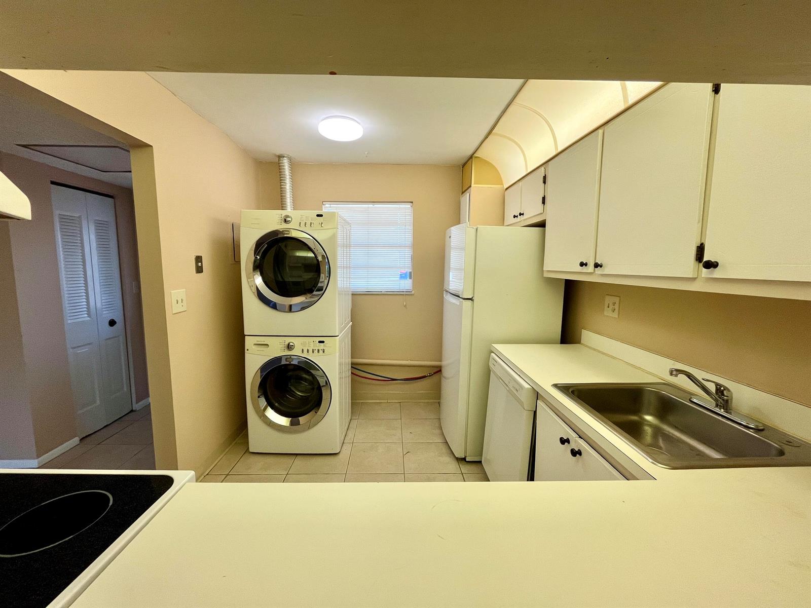 A kitchen features white cabinets, a stainless steel sink, a refrigerator, and a stacked washer-dryer — 2500 Fiore Way # 1110, Delray Beach FL 33445, DELRAY BEACH, FL