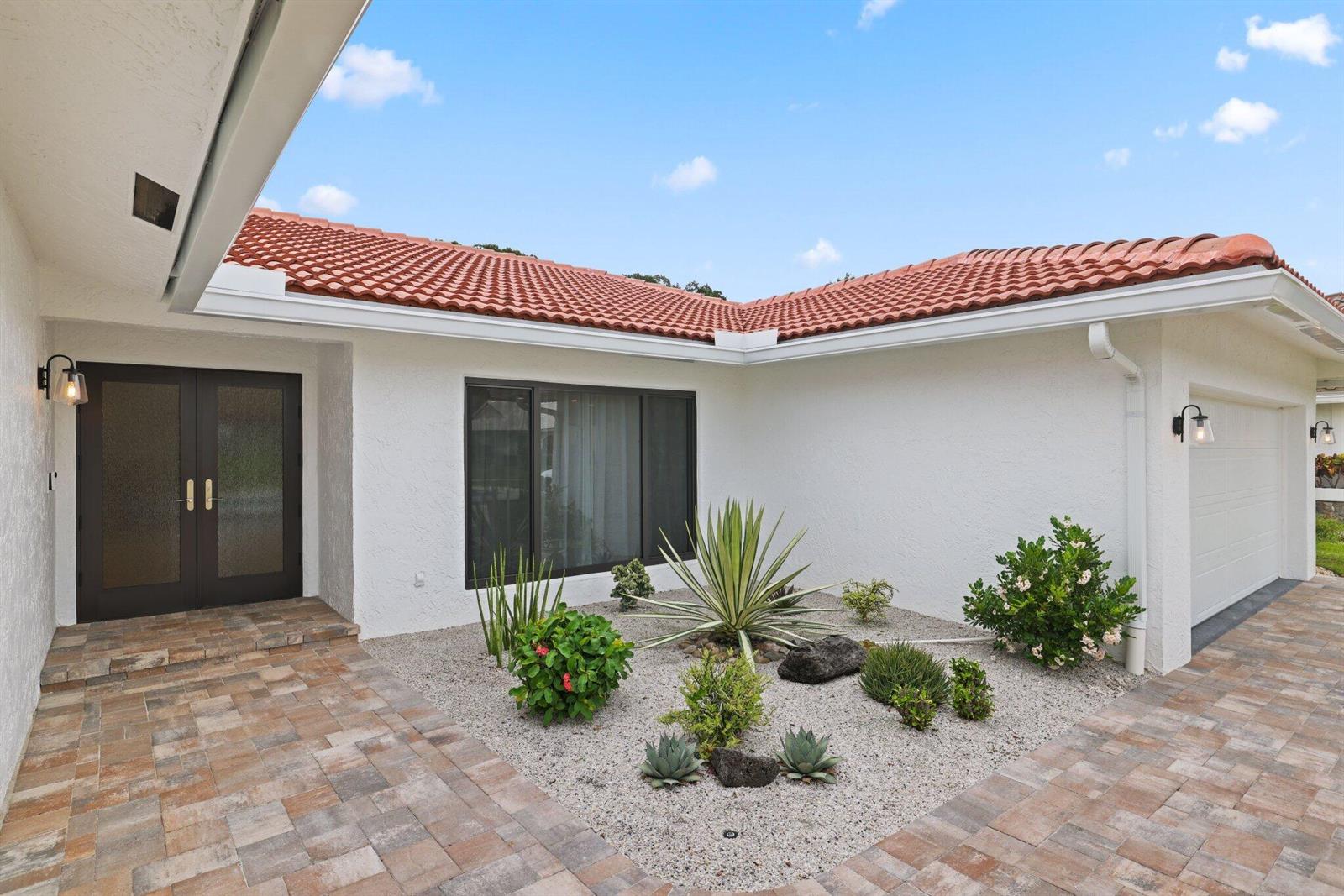 A white house exterior features a tiled roof, a paved walkway, and a rock garden — 20195 Back 9 Drive, Boca Raton FL 33498, BOCA RATON, FL