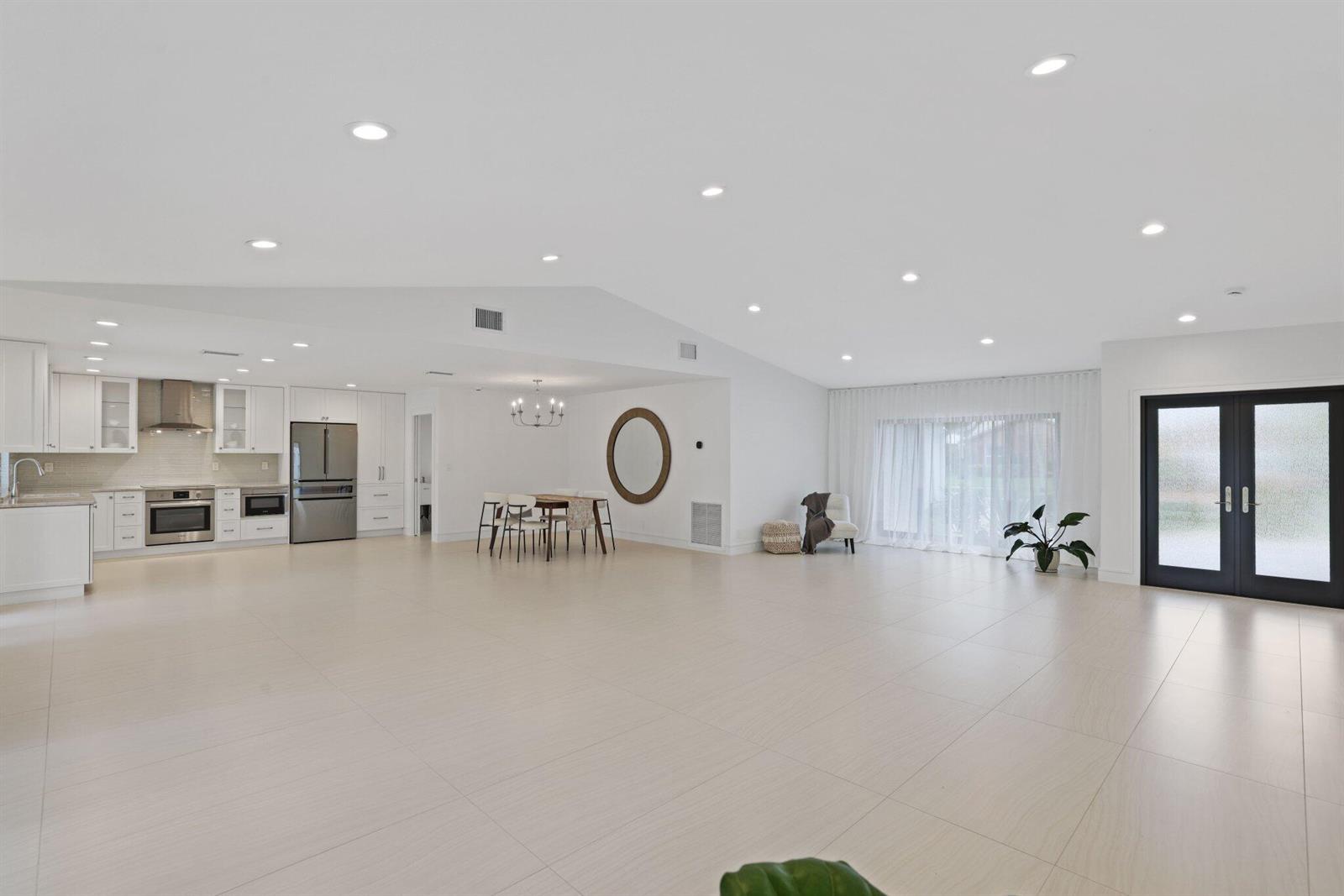 A spacious, open-concept kitchen and living area with white cabinetry, tile floors, and vaulted ceilings — 20195 Back 9 Drive, Boca Raton FL 33498, BOCA RATON, FL