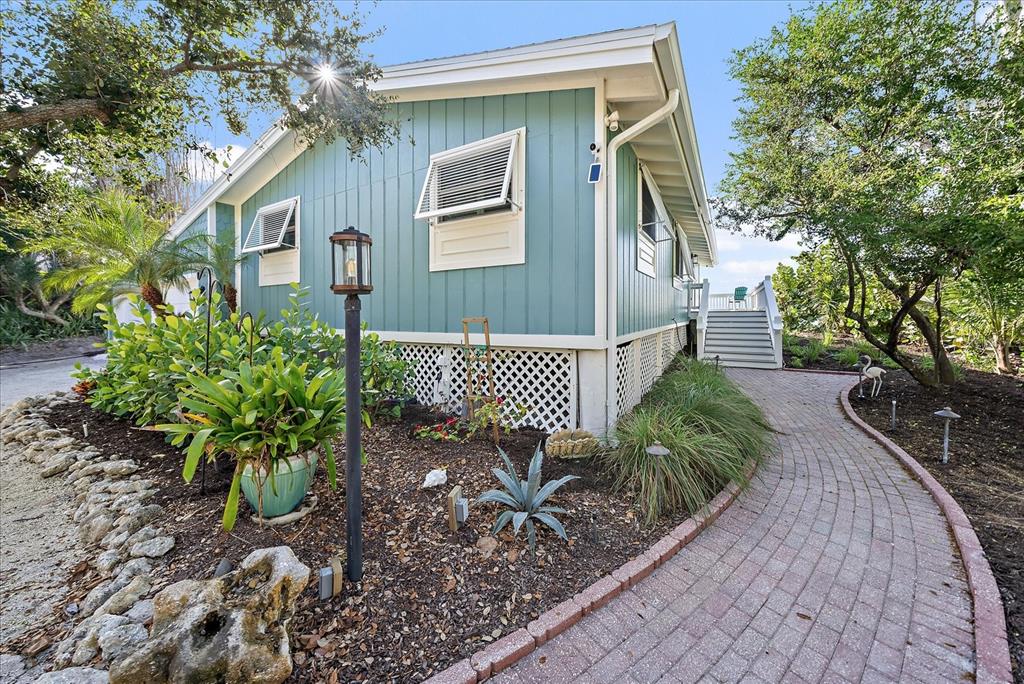 A teal house with white trim and lattice skirting sits beside a brick walkway — 7570 MANASOTA KEY ROAD, ENGLEWOOD, FL