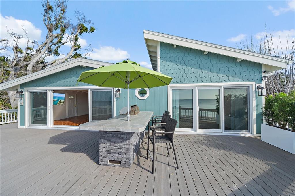 A teal house with a wooden deck, outdoor bar, and green umbrella overlooking the ocean — 7570 MANASOTA KEY ROAD, ENGLEWOOD, FL
