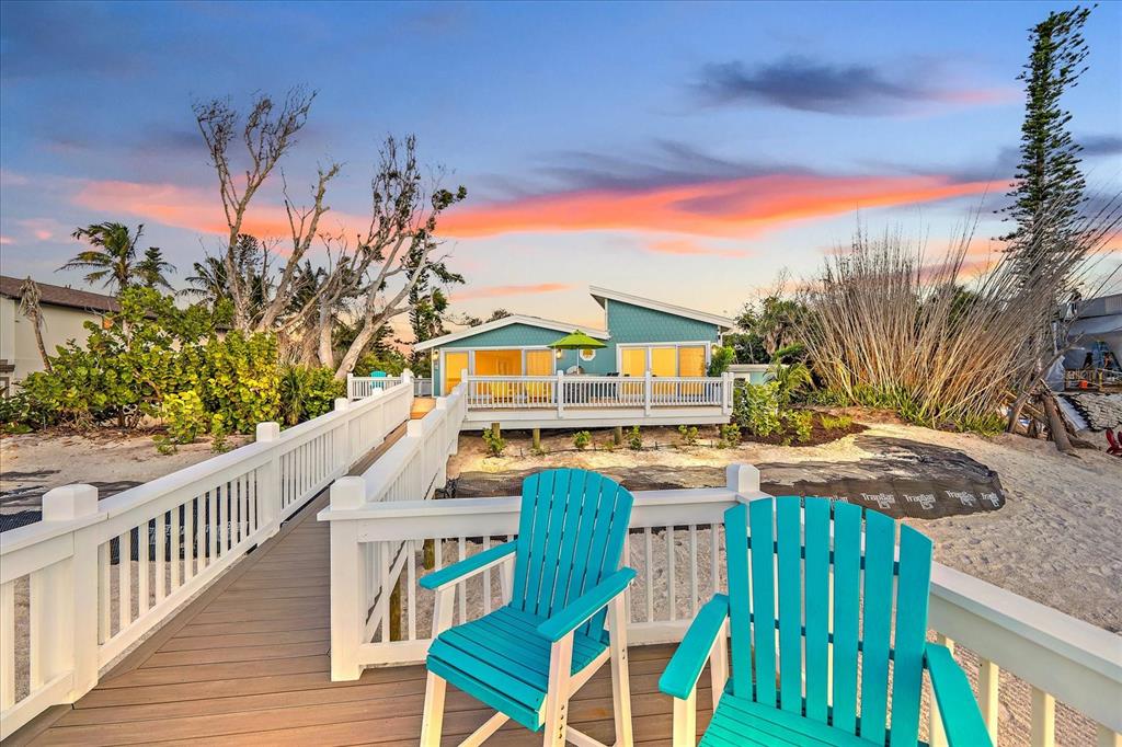 Two turquoise Adirondack chairs sit on a wooden deck leading to a coastal house exterior — 7570 MANASOTA KEY ROAD, ENGLEWOOD, FL